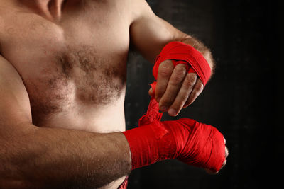 Midsection of shirtless boxer standing against black background