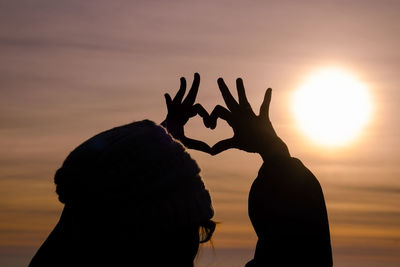 Silhouette woman making heart shape with hands against sky during sunset