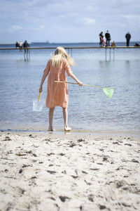 Rear view of woman standing on beach against sky