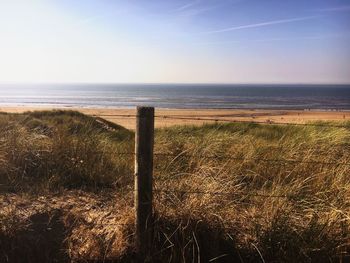 Fence on grassy beach against sky