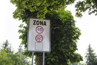 Information sign by trees against sky