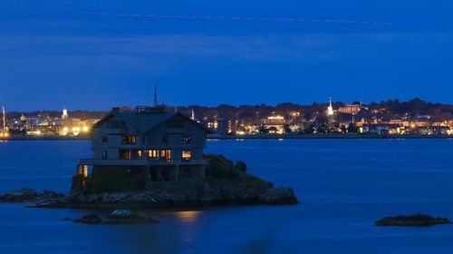 Illuminated buildings by sea against sky at dusk