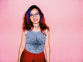 Portrait of smiling young woman standing against wall