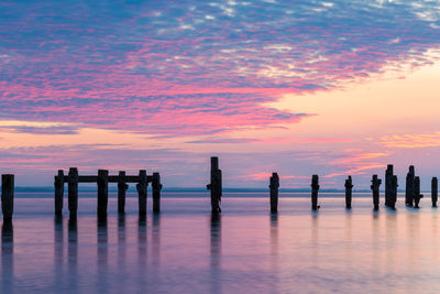 Silhouette wooden posts in sea against sky during sunset