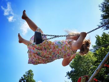 Low angle view of girl swinging against sky