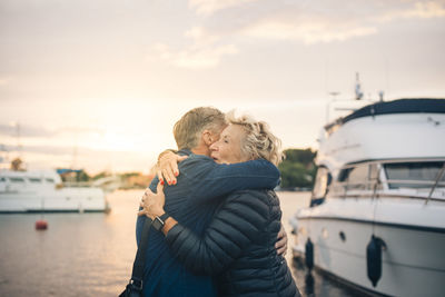 Side view of senior man and woman embracing at harbor during sunset