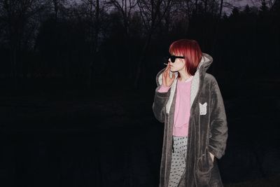 Woman looking away while standing against trees