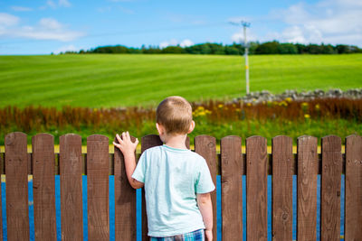 Rear view of boy standing by fence