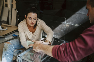 Man discussing and showing mobile phone to woman while renovating home