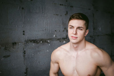 Shirtless muscular man standing by wall