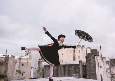 Woman holding umbrella while standing with arms outstretched on terrace