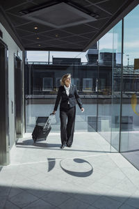 Mature businesswoman pulling wheeled luggage in hotel corridor