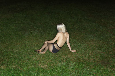 Rear view of topless young woman sitting on grassy field at night