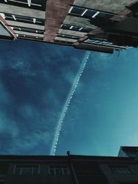 Directly below shot of vapor trail amidst buildings against sky