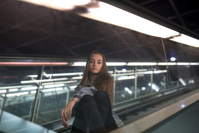 Portrait of young woman sitting on escalator seen through glass