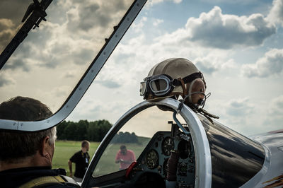 Rear view of pilot flying jet airplane on field against sky