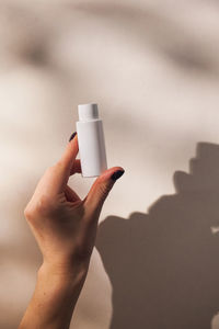 A tube of face and body care cosmetics in a woman's hand with hard shadows on the background. 