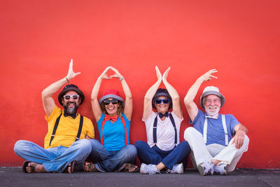 Portrait of smiling friends with arms raised sitting against red wall