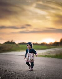Cute girl walking on road against cloudy sky during sunset