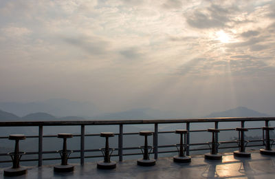 Seats on footbridge against sky during sunset