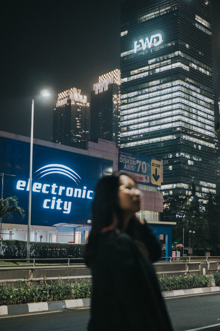 WOMAN STANDING AT ILLUMINATED CITY