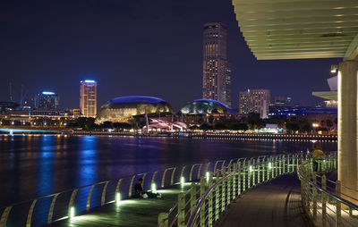 Illuminated bridge over river by buildings against sky at night