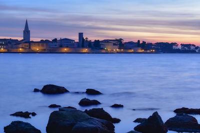 Sea by buildings against sky at sunset