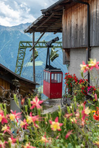 Red overhead cable car by building against sky