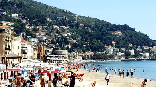 People at beach by city against mountain