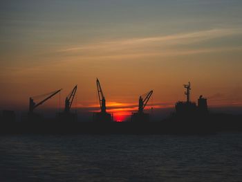 Silhouette cranes at commercial dock against sky during sunset