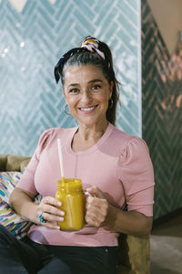 Happy woman sitting with fresh juice in mason jar at bar