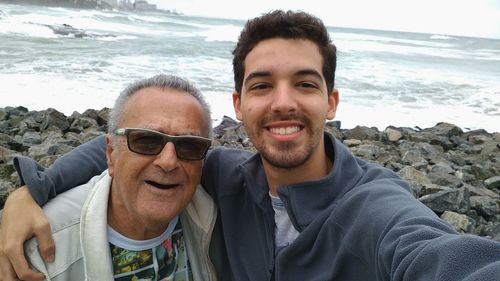 Portrait of young man with grandfather standing on rocky shore