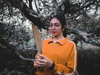 Young woman looking away while standing against tree