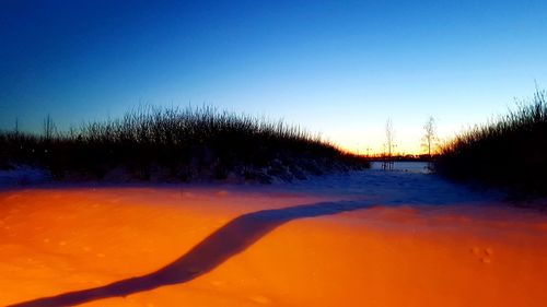 Scenic view of snow covered land against clear sky during sunset