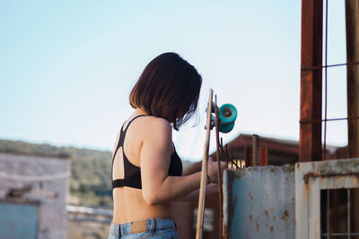 Woman with skateboard standing by wall against sky