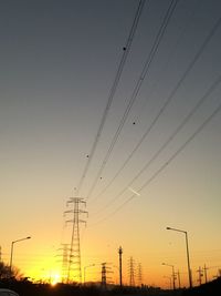 Low angle view of silhouette electricity pylons against clear sky