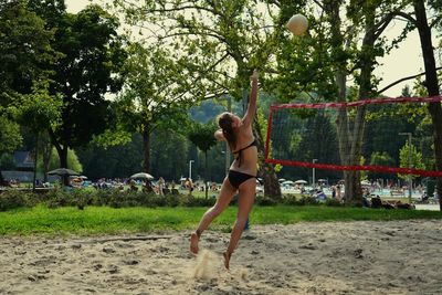 Full length of woman wearing bikini playing beach volleyball in park