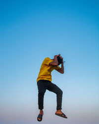 Side view of man photographing against clear blue sky