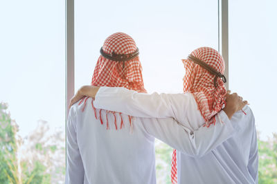 Rear view of men wearing dish dash by window