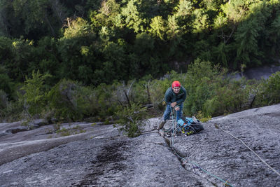 Man resting at belay and looking up at partner on multipitch climb