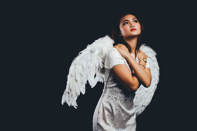 Young woman wearing angel wing against black background