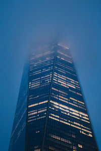 From below of modern high rise building with glowing windows located against foggy sky in new york city in evening time