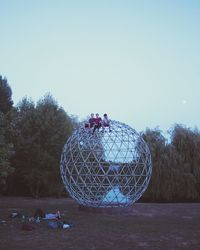 People on field by trees against clear sky