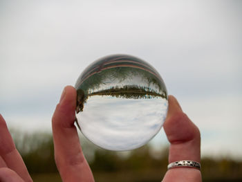 Cropped image of hand holding crystal ball against sky