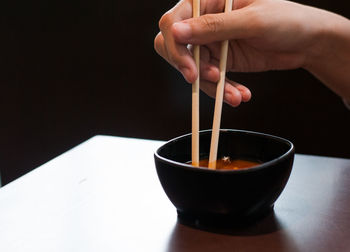 Close-up of hand holding tea cup against black background