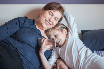 Grandmother and grandson looking at mobile phone while on bed at home