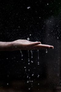 Close-up of hand with splashing water against black background