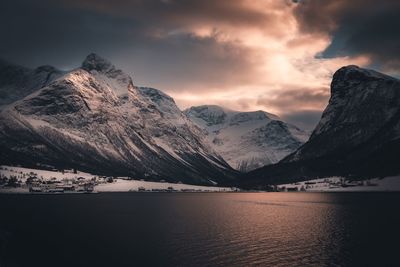 Scenic view of lake by snowcapped mountains against sky during sunset