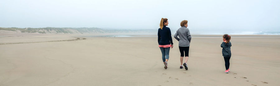 Panoramic view of people walking at beach against sky