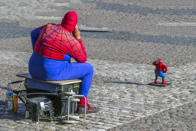 Person in superman costume with figurine sitting on road in city